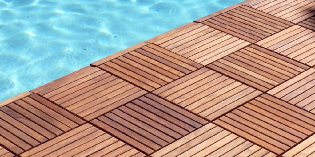 Close-up of interlocking wooden deck tiles laid in a pattern next to the bright blue water of a swimming pool